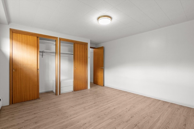 unfurnished bedroom with light wood-style floors, baseboards, and multiple closets