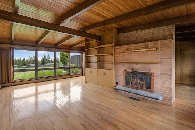 unfurnished living room featuring wood walls, visible vents, light wood-style floors, a brick fireplace, and beam ceiling