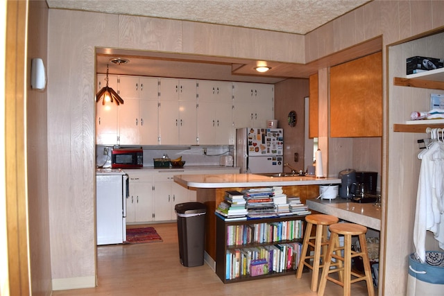 kitchen with a breakfast bar, sink, white cabinetry, white appliances, and light hardwood / wood-style floors