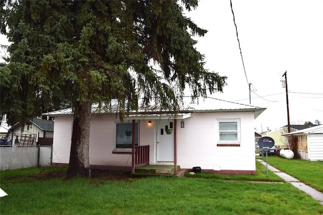view of front of property with concrete block siding, fence, a front yard, and metal roof