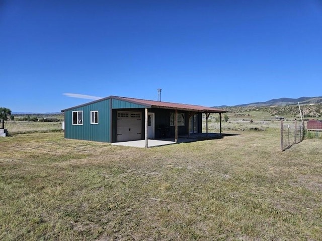 back of property featuring a mountain view, a garage, an outbuilding, a yard, and a rural view