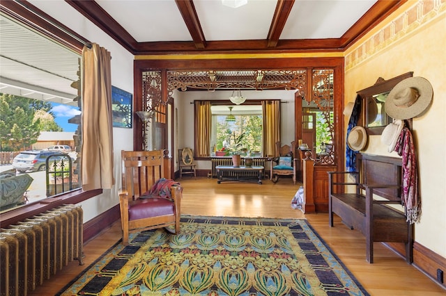 living area featuring radiator heating unit, beamed ceiling, light hardwood / wood-style floors, and ornamental molding