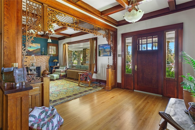 foyer featuring light wood-type flooring, a brick fireplace, radiator, coffered ceiling, and beamed ceiling