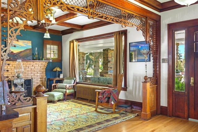 living area featuring radiator, coffered ceiling, a brick fireplace, hardwood / wood-style flooring, and beamed ceiling