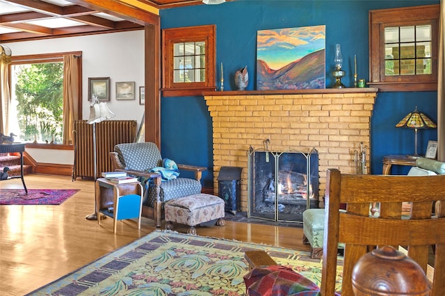 living area with hardwood / wood-style floors, coffered ceiling, a brick fireplace, beam ceiling, and radiator heating unit