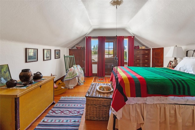 bedroom featuring a textured ceiling, light hardwood / wood-style floors, and lofted ceiling