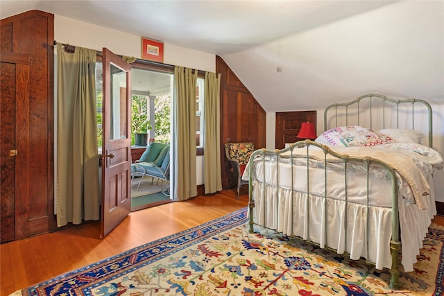 bedroom with access to outside, wood-type flooring, and vaulted ceiling