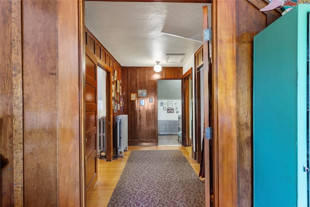 corridor with wood walls, light hardwood / wood-style floors, a textured ceiling, and radiator heating unit