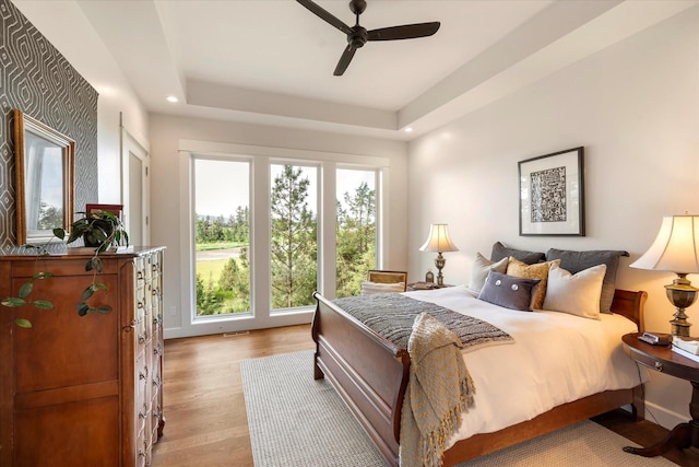 bedroom with a raised ceiling, ceiling fan, and light hardwood / wood-style floors