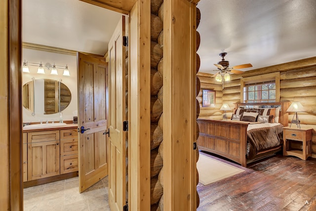 bedroom featuring ceiling fan, light hardwood / wood-style flooring, ensuite bath, rustic walls, and sink