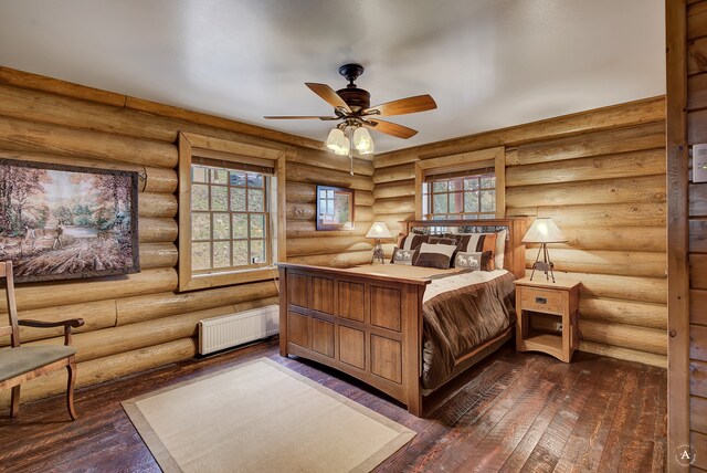 bedroom featuring dark wood-type flooring, radiator heating unit, log walls, and ceiling fan