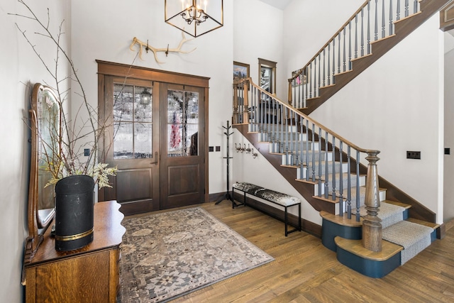 entrance foyer with wood finished floors, a towering ceiling, baseboards, stairs, and an inviting chandelier