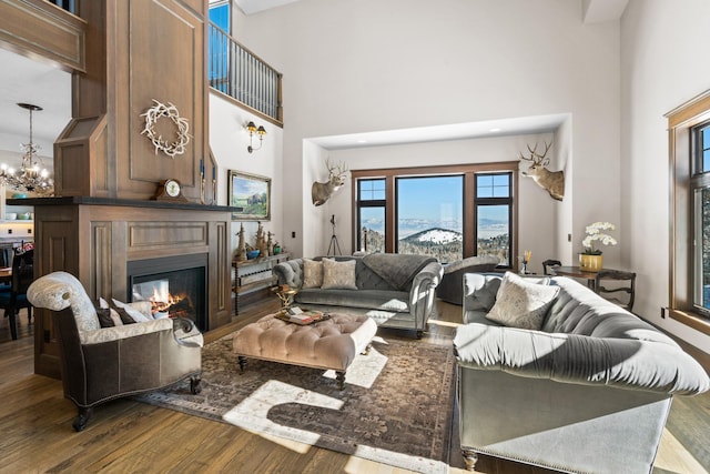 living area featuring a high ceiling, an inviting chandelier, a glass covered fireplace, a mountain view, and wood finished floors