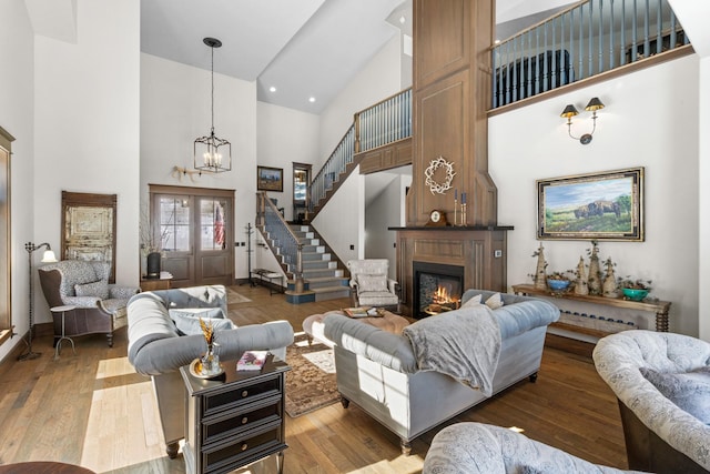 living area featuring stairway, a high ceiling, a glass covered fireplace, wood finished floors, and a chandelier