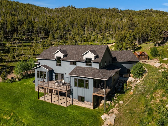 back of property with board and batten siding, a deck, and a wooded view