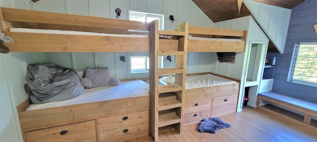 bedroom with light wood-style floors, wooden walls, and vaulted ceiling