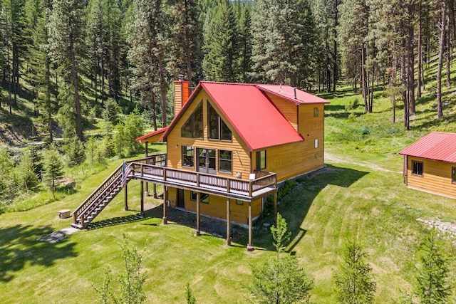 back of house featuring a wooded view, a wooden deck, a chimney, stairway, and a lawn