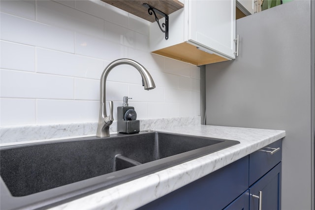 kitchen featuring tasteful backsplash, sink, blue cabinetry, stainless steel refrigerator, and light stone counters