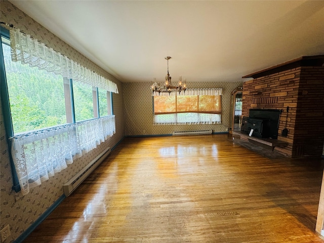 interior space with a chandelier, wood-type flooring, a baseboard radiator, and a stone fireplace