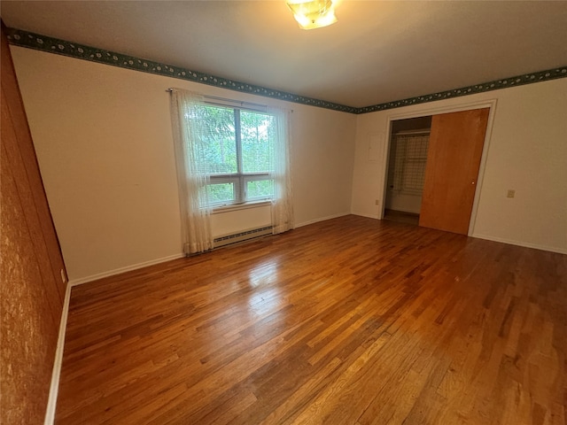 spare room featuring baseboard heating and hardwood / wood-style flooring