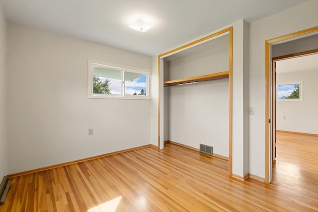 unfurnished bedroom featuring hardwood / wood-style flooring, baseboard heating, and a closet