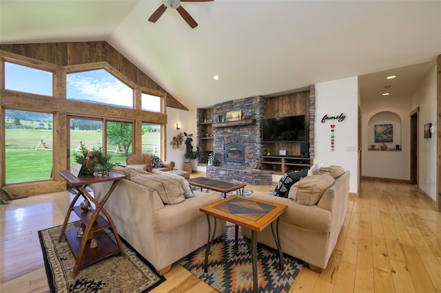 living room with a fireplace, light wood-type flooring, built in shelves, high vaulted ceiling, and ceiling fan