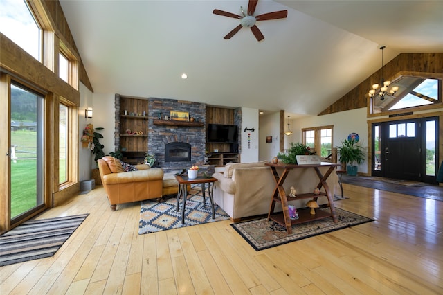 living room with a fireplace, ceiling fan with notable chandelier, high vaulted ceiling, built in features, and light hardwood / wood-style floors