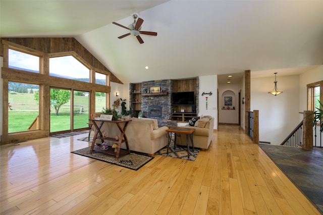 living room featuring ceiling fan, a fireplace, light wood-type flooring, and high vaulted ceiling