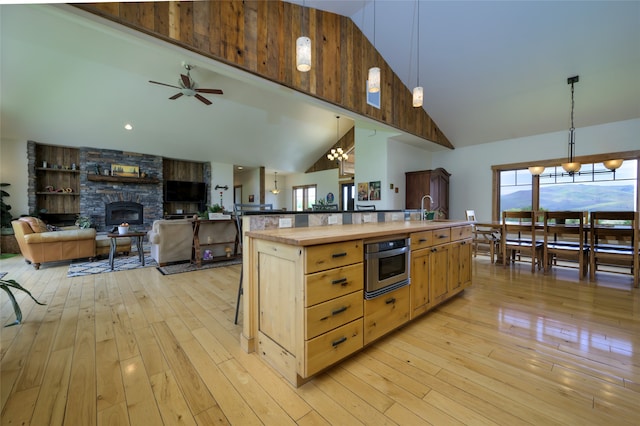 kitchen featuring an island with sink, hanging light fixtures, light wood-type flooring, and high vaulted ceiling