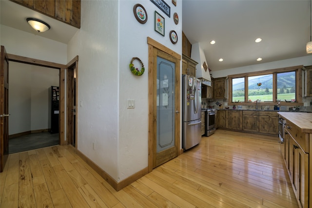 kitchen with appliances with stainless steel finishes, light hardwood / wood-style flooring, tasteful backsplash, sink, and lofted ceiling