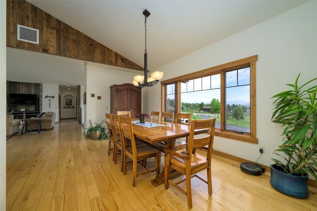 dining space with high vaulted ceiling, an inviting chandelier, and light wood-type flooring