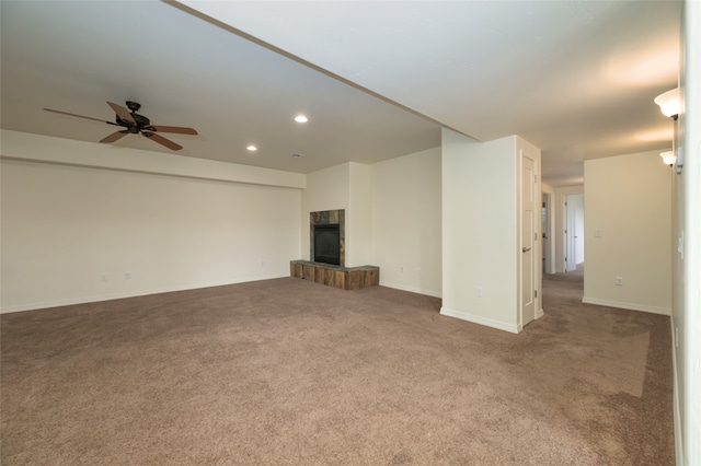 unfurnished living room with a tile fireplace, dark colored carpet, and ceiling fan