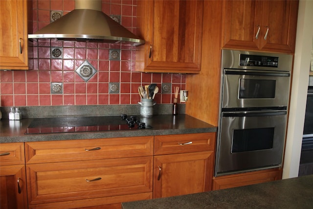 kitchen with backsplash, black electric cooktop, double oven, and wall chimney range hood