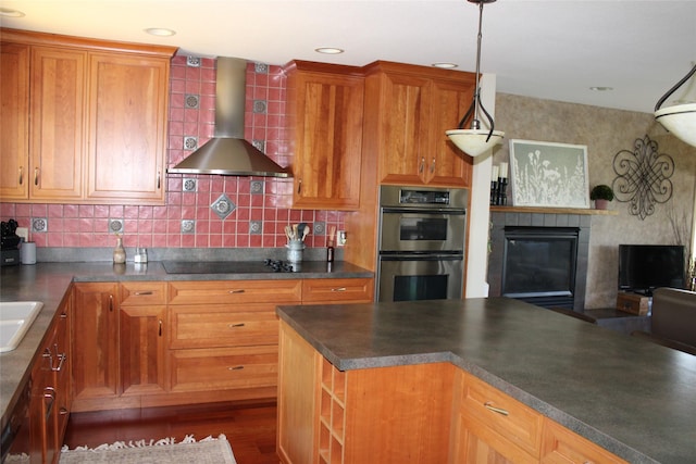 kitchen featuring a tile fireplace, wall chimney exhaust hood, stainless steel double oven, hanging light fixtures, and black electric cooktop