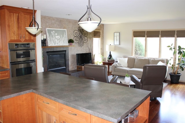 kitchen with stainless steel double oven, dark wood-type flooring, and hanging light fixtures