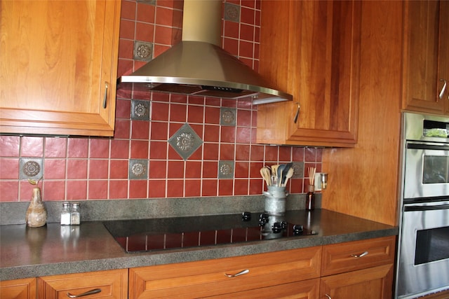 kitchen with stainless steel double oven, black electric cooktop, tasteful backsplash, and wall chimney range hood