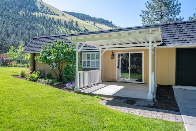 rear view of property featuring mansard roof, a shingled roof, a lawn, a patio area, and a mountain view