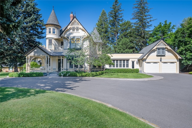 victorian home with driveway, a garage, a balcony, a porch, and a front lawn