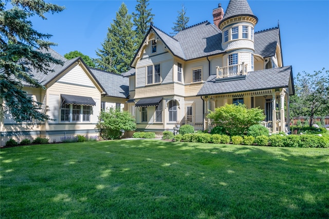 victorian home with a chimney, a front yard, and a balcony