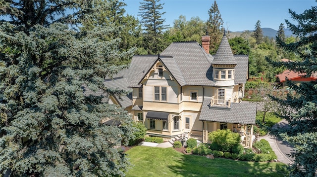 view of front facade featuring a balcony, a tile roof, a chimney, a porch, and a front yard