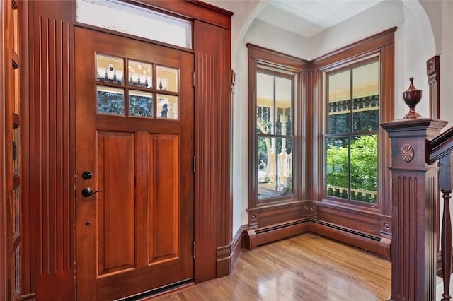 entryway with light wood-type flooring, arched walkways, and baseboard heating