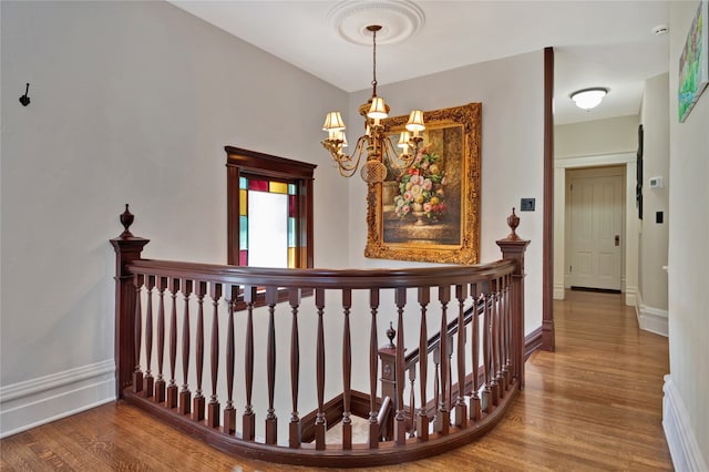 hall with baseboards, a chandelier, and wood finished floors