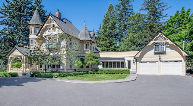 victorian house with a garage, driveway, a chimney, and a front lawn