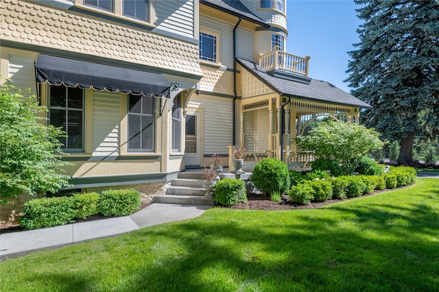 view of exterior entry with a lawn and a balcony