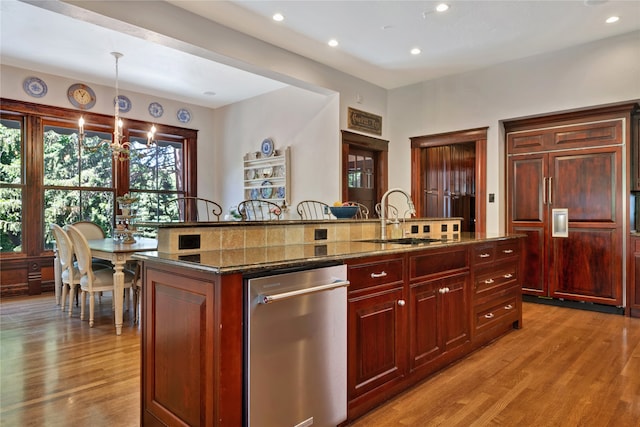 kitchen with paneled built in refrigerator, a sink, dark stone countertops, wood finished floors, and dark brown cabinets