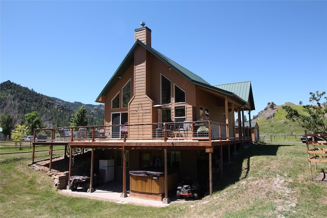 back of property with a deck with mountain view, a chimney, fence, and a hot tub