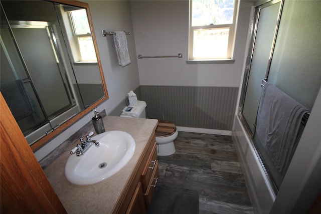 bathroom with toilet, a wainscoted wall, wood finished floors, combined bath / shower with glass door, and vanity