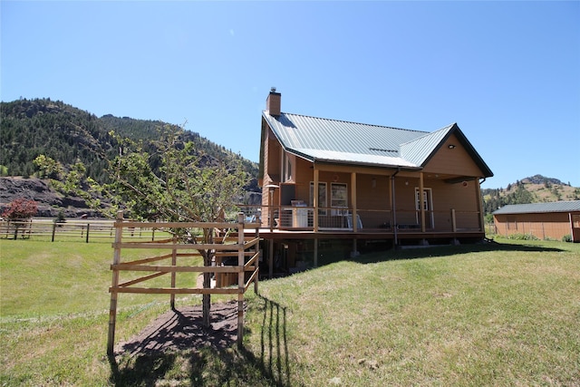 rear view of house featuring a chimney, fence, metal roof, and a lawn