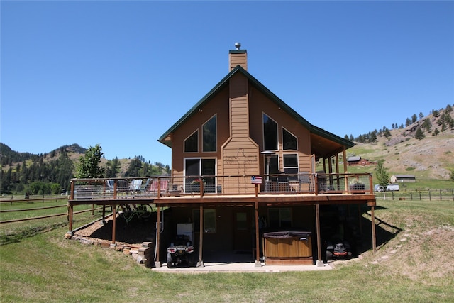 back of property featuring a chimney, a deck with mountain view, a hot tub, fence, and a rural view