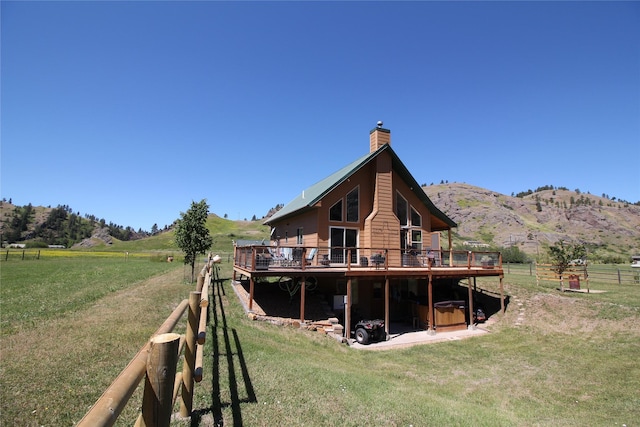 back of property with a deck with mountain view, a rural view, fence, a yard, and a chimney